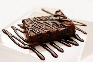 brownie on a white plate with chocolate syrup on top 