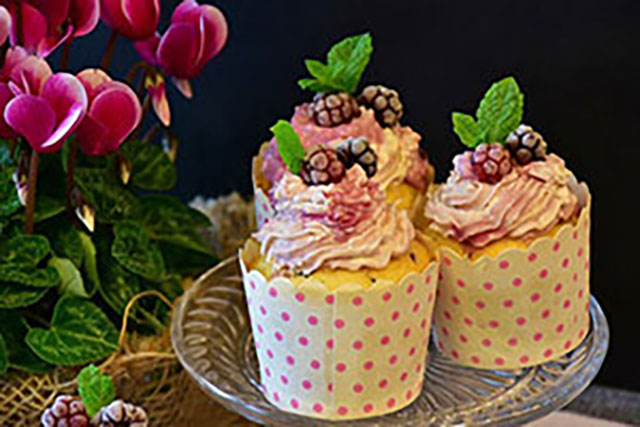 Three decorated vanilla and berry cupcakes on a glass platter